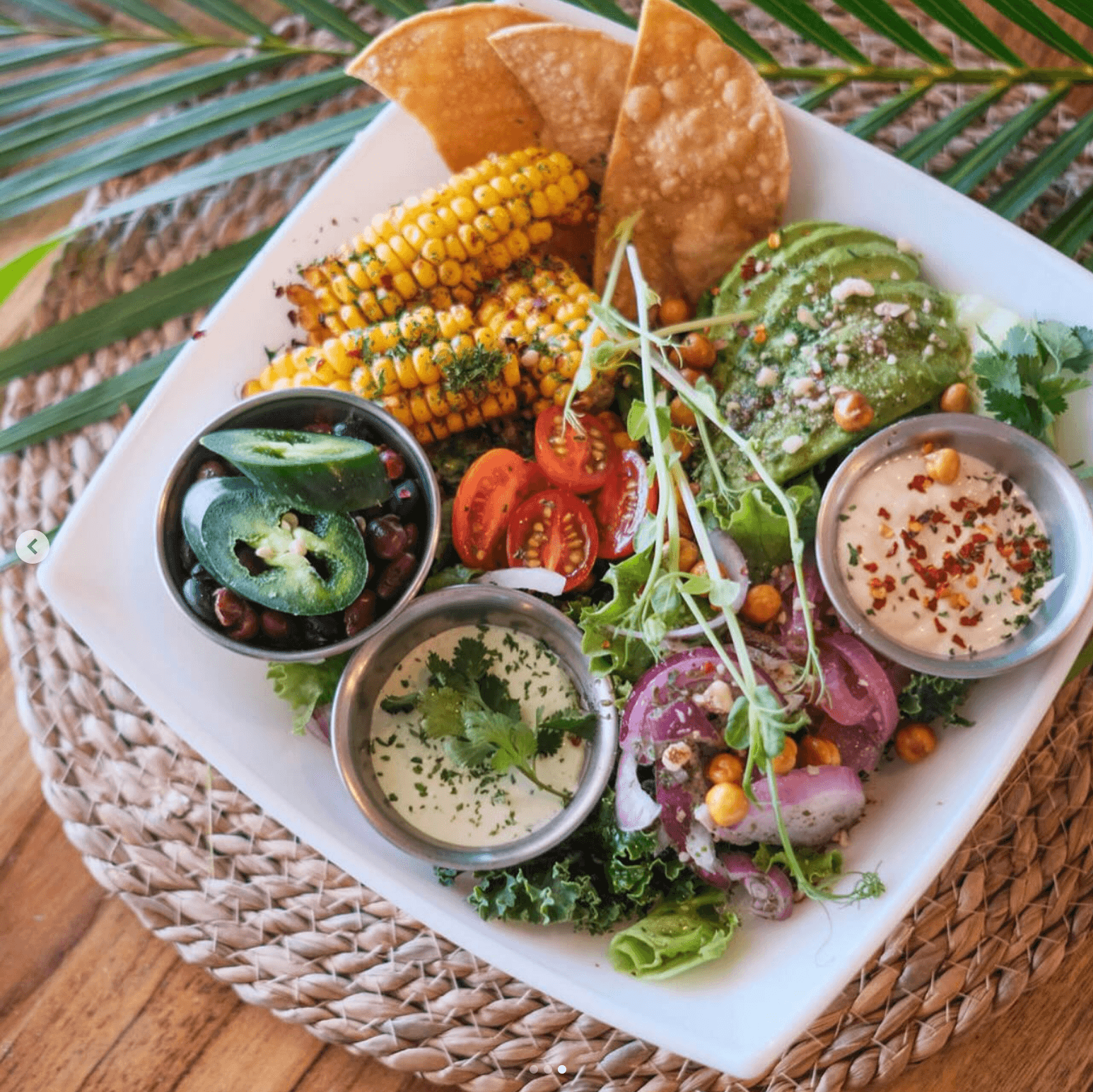 Karma plant-based taco bowl with grilled corn, avocado, tomato, and fresh greens on a palm-leaf table setting